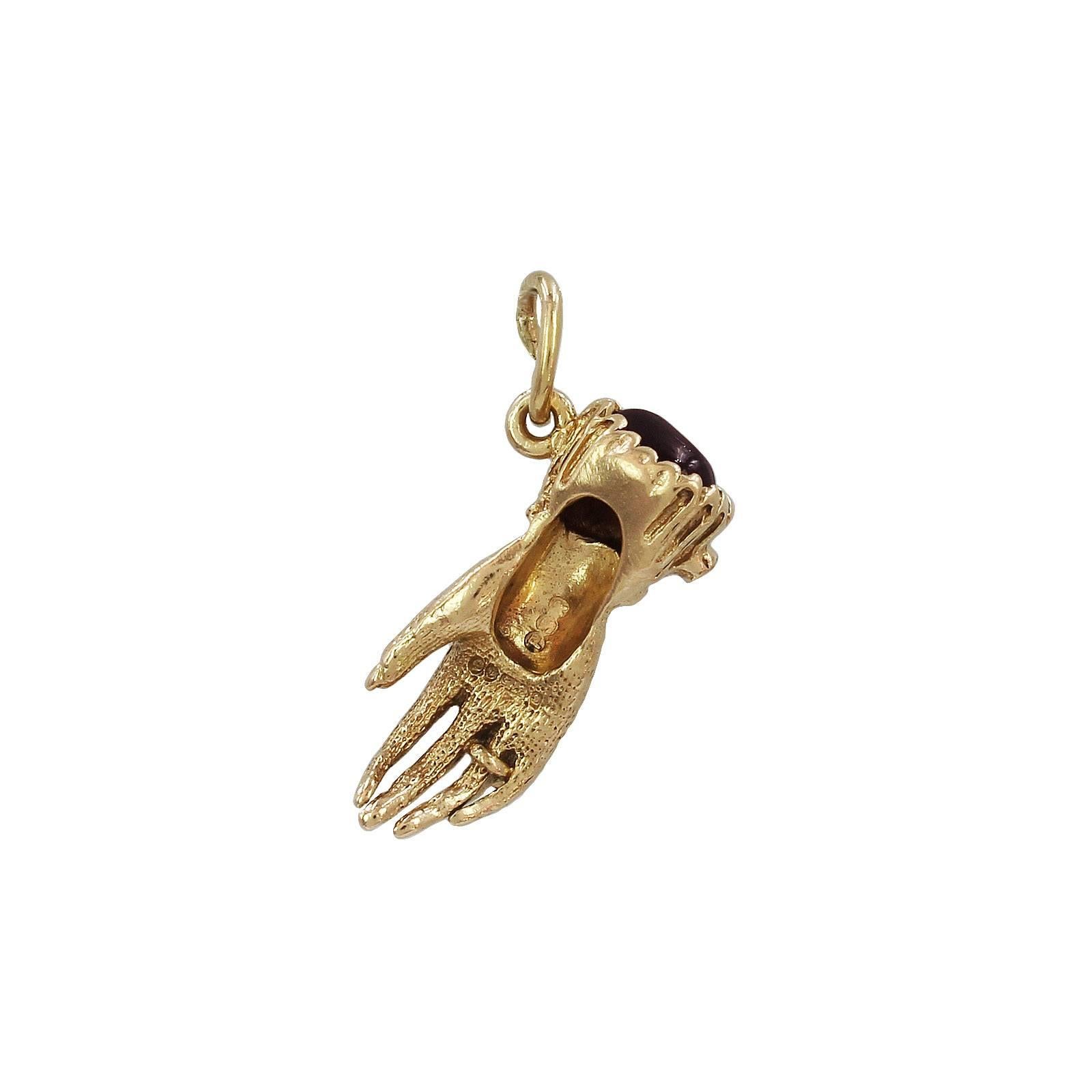 A 9k gold figa gem set pendant. In the form of a hand wearing a ring, with frilled cuff set with a blue gem and a red gem cabochon to the terminal. Hallmark for London, 1974. Length 2.2cms. Weight 2.9gms.