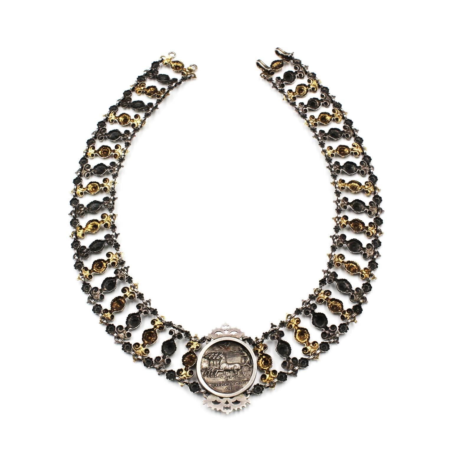 An Austro-Hungarian 19th century silver collar necklace by Georg Adam Scheid, formed from a line of silver and silver gilt foliate scroll links joined by a floral border to each end. The front section mounted with an ancient silver tetradrachma coin