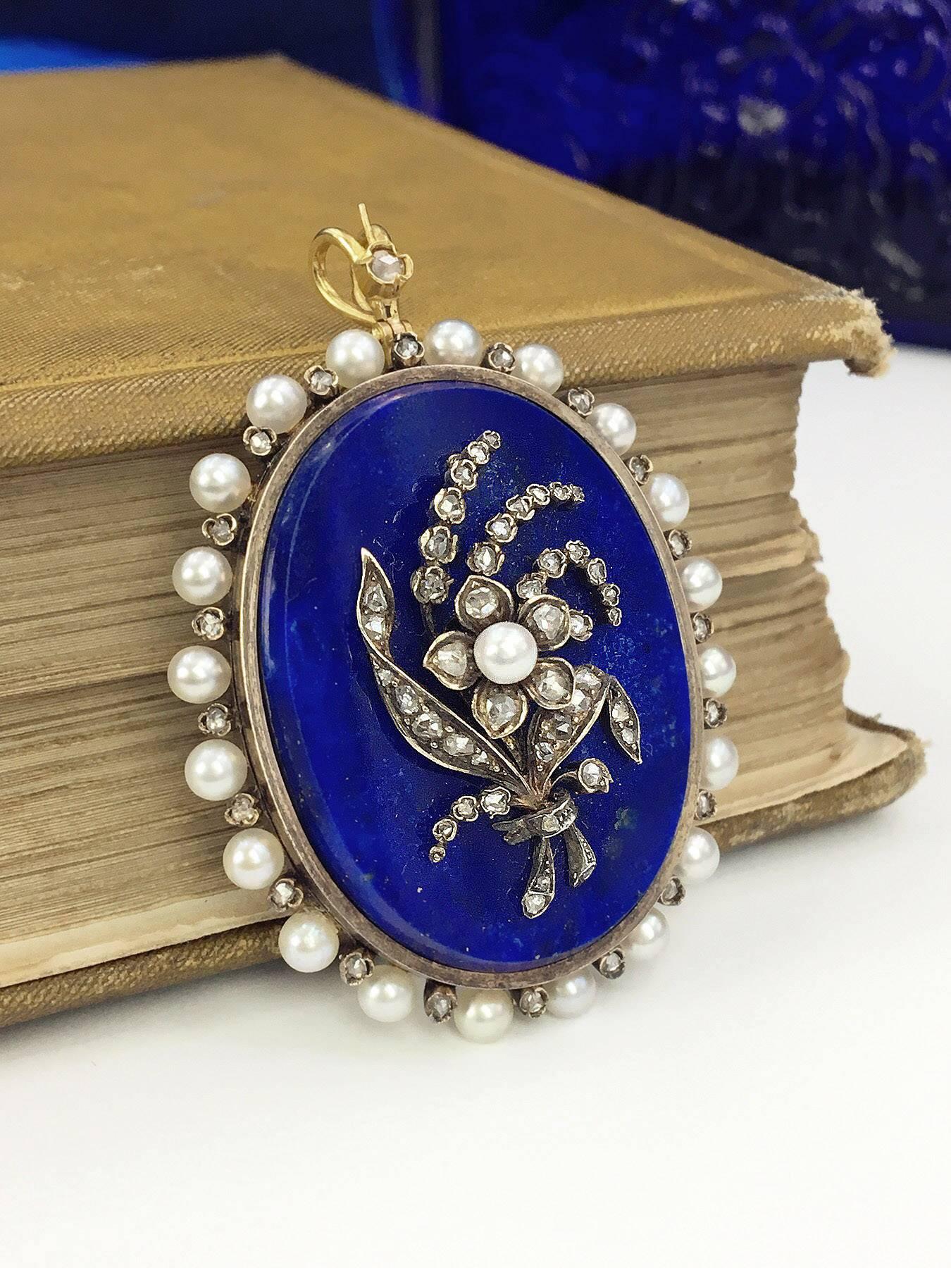 An early 20th century lapis lazuli and gem-set pendant. The rose-cut diamond and seed pearl floral motif, atop the oval lapis lazuli disc, with rose-cut diamond and seed pearl surround. Length 5cms. Weight 21.2gms.