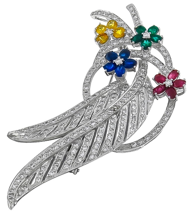 Made of 14k white gold, this pin is set with sparkling round cut diamonds  weighing approximately 4.00ct. The diamonds are accentuated by round and oval cut yellow sapphires, blue sapphires, emeralds and rubies that weigh approximately 7.50ct.