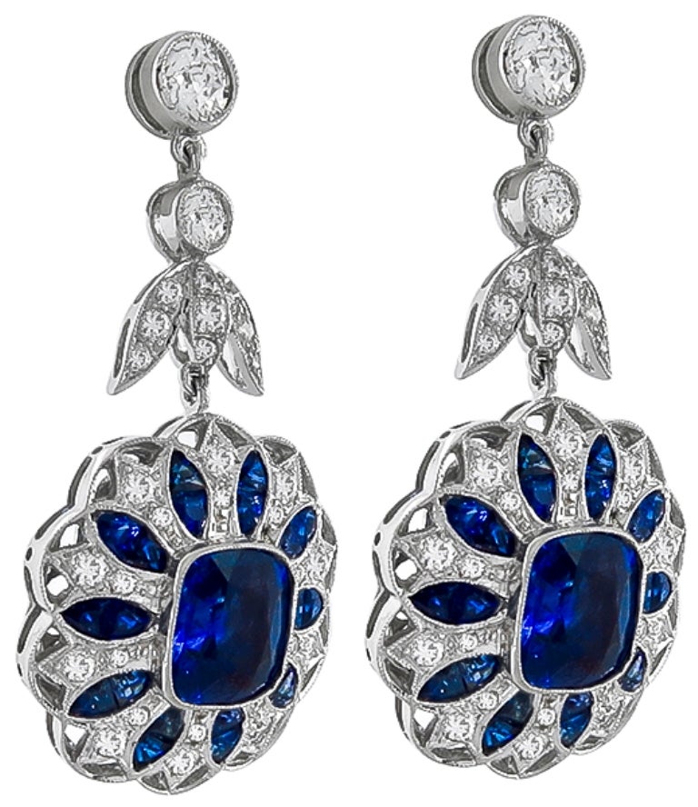 Made of 18k white gold, these earrings are set with vivid blue cushion and faceted cut sapphires that weigh approximately 9.90ct. The sapphires are accentuated by sparkling old mine and round cut diamonds that weigh approximately 2.30ct. The color