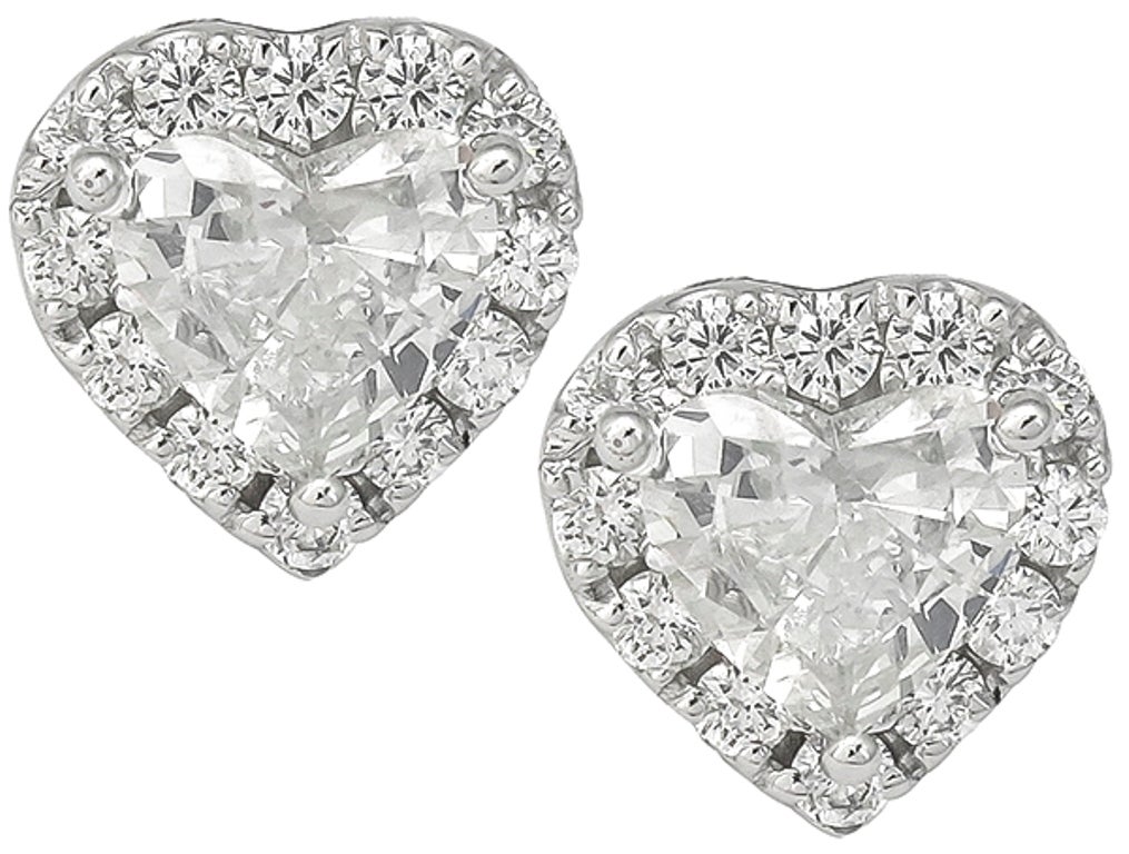 This stunning pair of 18k white gold earrings are centered with sparkling heart shaped diamonds that weigh 2.05ct. The color of these diamonds is I with SI2 clarity. The center stones are accentuated by dazzling round cut diamonds that weigh
