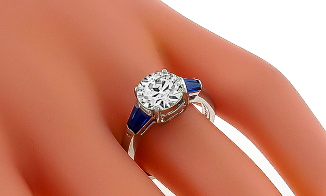 This gorgeous platinum engagement ring, centers a sparkling old mine cut diamond that weighs 2.02ct. and is graded K-L color with VS1 clarity. The center stone is flanked by vivid blue baguette cut sapphire accents. 
The ring is stamped Angelo &