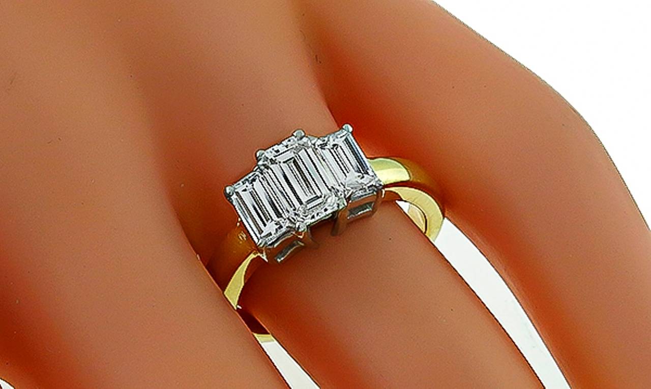 Made of 18k yellow and white gold, this ring centers a sparkling GIA certified emerald cut diamond that weighs 1.05ct. and is graded H color with VVS1 clarity. The center diamond is adorned with 2 emerald cut diamonds weighing approximately 1.00ct.