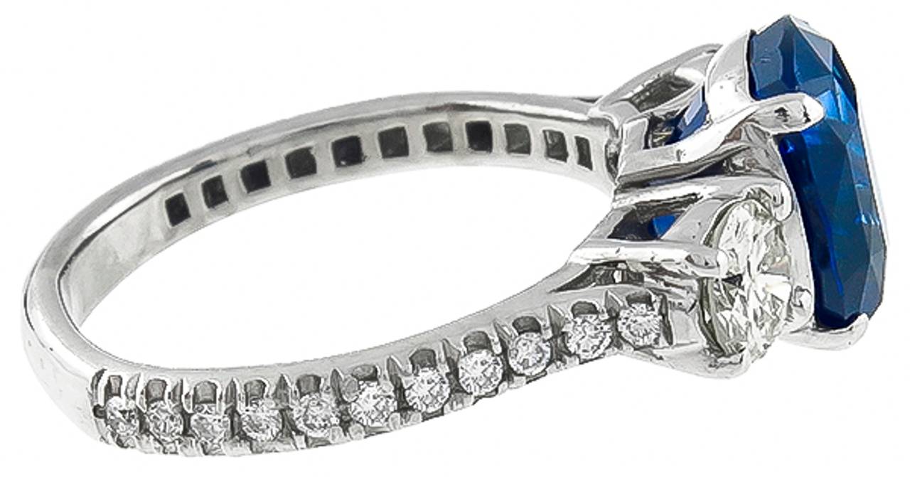 This stunning platinum engagement ring centers a vivid blue cushion cut Ceylon sapphire that weighs 4.04ct. The center stone is accentuated by two large sparkling round cut diamonds that weigh approximately 0.65ct. graded G color with VS clarity and