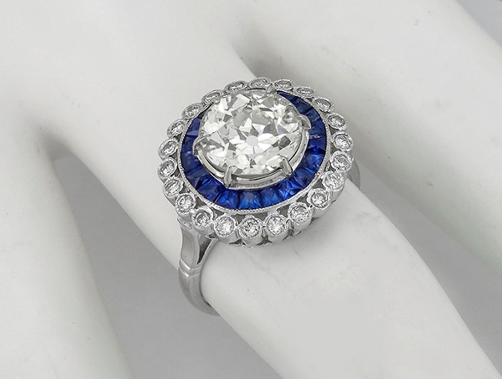 Made of 14k white gold, this ring centers a sparkling EGL certified old European cut diamond that weighs 2.58ct.and is graded J-K color with SI3 clarity. The center stone is accentuated by vivid blue french cut sapphires that weigh approximately