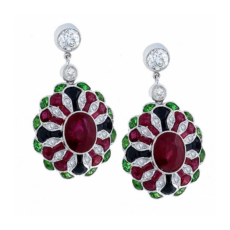 This is an elegant pair of sapphire diamond tsavorite and onyx 18k white gold earrings inspired from the Art Deco period. The earrings feature deep red oval and faceted cut rubies that weigh approximately 5.97ct. The rubies accentuated by faceted