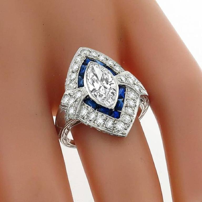 Made of platinum, this ring centers a sparkling GIA certified marquise cut diamond that weighs 1.18ct. graded F color with SI1 clarity. Accentuating the center stone are French cut sapphires that weigh approximately 0.40ct. and round cut diamonds