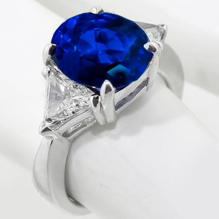 This stunning 14K white gold ring is set with a natural vivid blue oval cut sapphire that weighs 4.12ct. The sapphire is flanked by 2 sparkling trilliant cut diamonds that weigh approximately 0.75ct. graded H color with VS clarity. 
The ring is