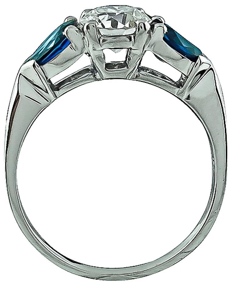 This platinum ring is centered with a sparkling GIA certified round cut diamond that weighs 0.88ct. graded I color with VS1 clarity. The center stone is flanked by two pear shaped sapphires weighing approximately 0.70ct. The top of the ring measures
