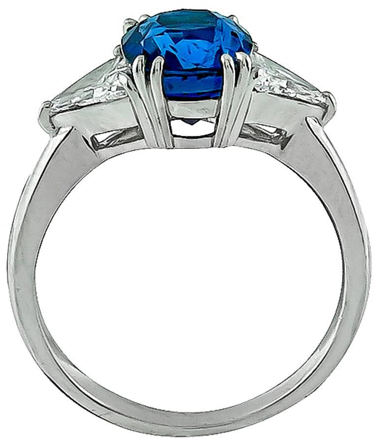 This elegant platinum ring is centered with a lovely cushion cut Ceylon sapphire that weighs 4.00ct. The center stone is flanked by sparkling trilliant cut diamonds that weigh approximately 1.00ct. graded G-H color with VS2 clarity. 
The ring is