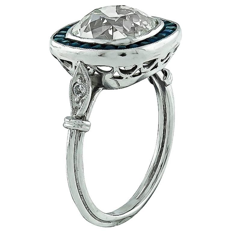 This stunning antique engagement ring from the Art Deco era, is centered with a sparkling cushion cut diamond that weighs 3.42ct. graded  K color with VS1 clarity. The center stone is accentuated by lovely sapphire accents.
The ring is currently