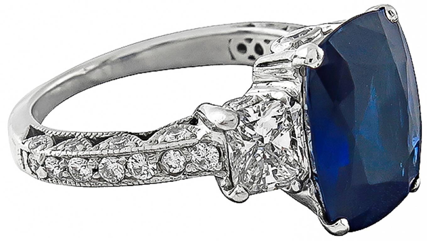 Made of platinum, this ring centers a natural cushion cut vivid blue sapphire that weighs 3.99t. Accentuating the sapphire are two radiant cut diamonds weighing approximately .70ct. and small round cut diamonds weighing approximately .40ct. The