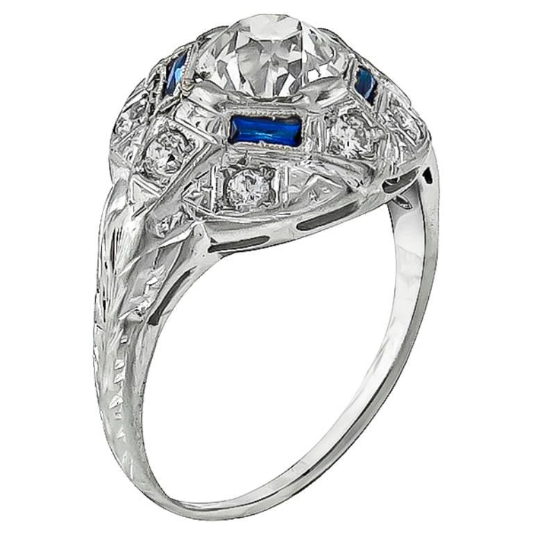 This amazing platinum engagement ring from the Art Deco era, is centered with a sparkling old mine cut diamond that weighs 1.10ct. graded J-K color with VS1 clarity. The center stone is accentuated by lovely sapphire and diamond accents. It is size