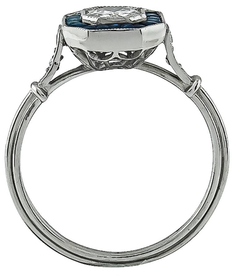 This elegant platinum ring is centered with a sparkling round cut diamond that weighs approximately 0.50ct. graded F-G color with VS2 clarity. The center diamond is accentuated by french calibre cut sapphires and round cut diamond accents. 
The