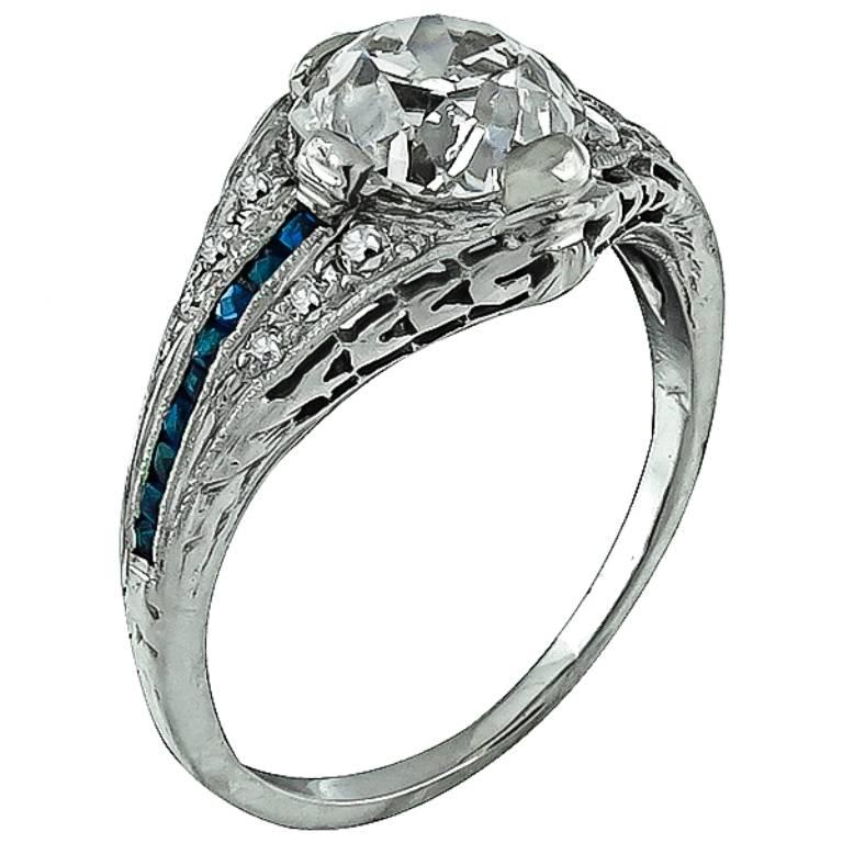 This magnificent platinum engagement ring is centered with a sparkling old mine cushion cut diamond that weighs 1.28ct. and is graded I color with SI1 clarity. The center stone is accentuated by sapphire and diamond accents. 
The ring is currently