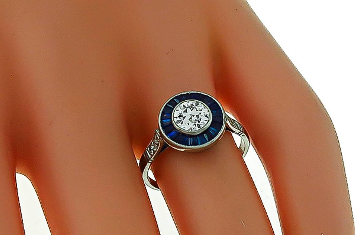 Hergestellt aus Platin, ist dieser Ring mit einem funkelnden GIA-zertifizierten runden Brillantschliff Diamant, der 0,70ct wiegt zentriert. graded H Farbe mit VS1 Klarheit. Der Mittelstein wird von gleichmäßig gefärbten Saphiren im Kaliberschliff