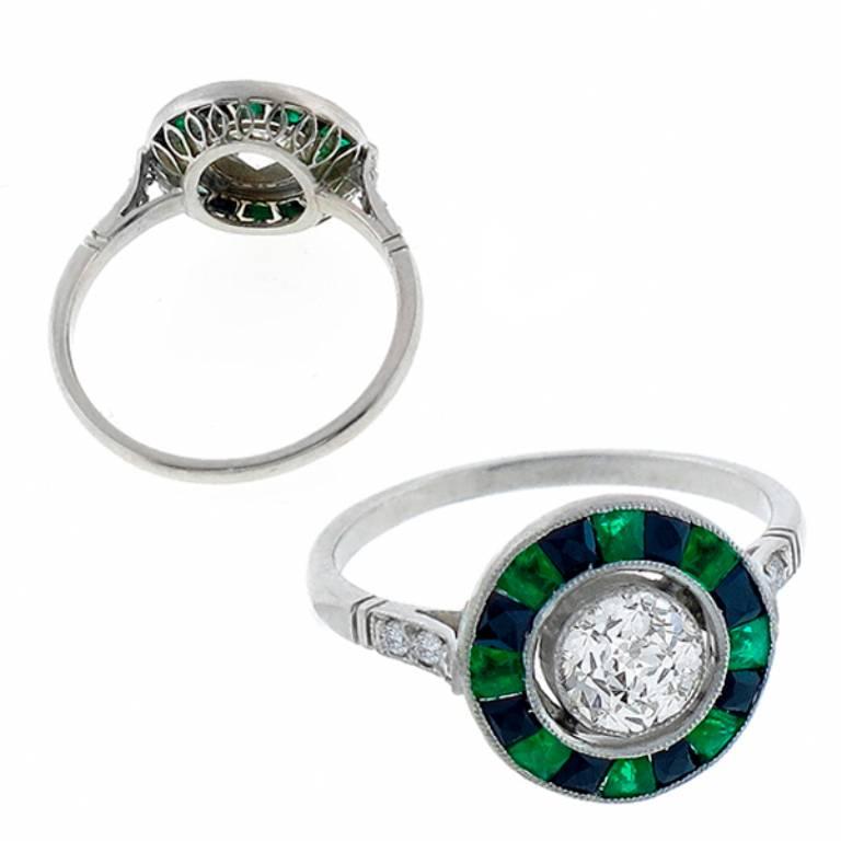 Made of platinum, this ring is centered with a sparkling GIA certified old European brilliant cut diamond that weighs 0.64ct. graded J color with VS2 clarity. Accentuating the center stone are high quality calibre cut emeralds,  onyx, and round cut