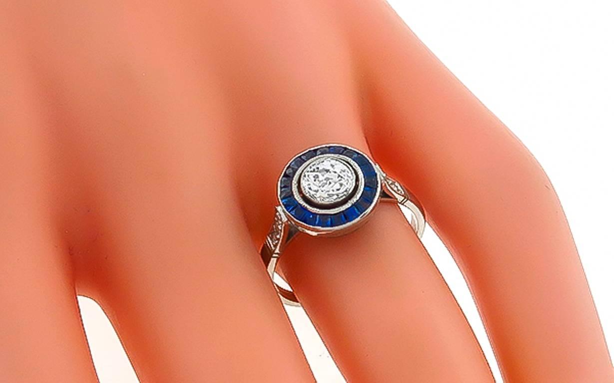 This elegant platinum ring is centered with a sparkling GIA certified old mine brilliant cut diamond that weighs 0.62ct. graded I color with VS1 clarity. Accentuating the center stone are even colored french calibre cut sapphires and rose cut