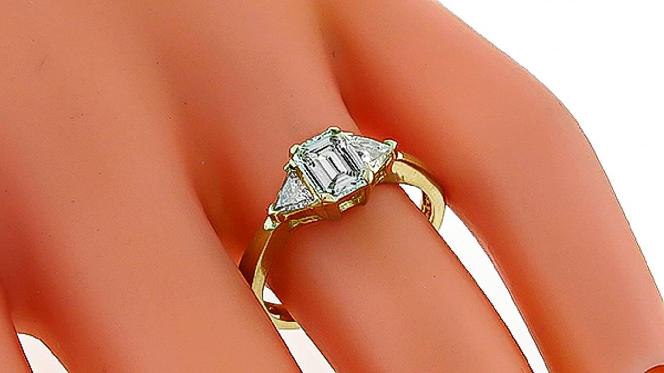 Dieser Ring aus 14 Karat Gelbgold enthält einen funkelnden Diamanten im Smaragdschliff mit einem Gewicht von 0,69 ct. und einer Graduierung. Farbe G mit Reinheit VS1. Der zentrale Diamant wird von zwei Diamanten im Trilliant-Schliff flankiert, die