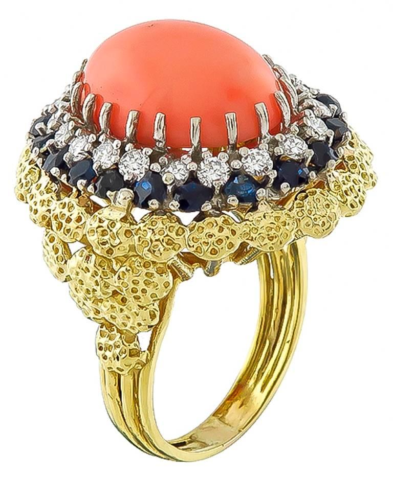 Made of 18k yellow gold, this ring centers with a high quality cabochon oval cut coral. Accentuating the coral are round cut sapphires weighing approx 1.75ct and sparkling round cut diamonds weighing approx 1ct. graded G color with VS clarity. The
