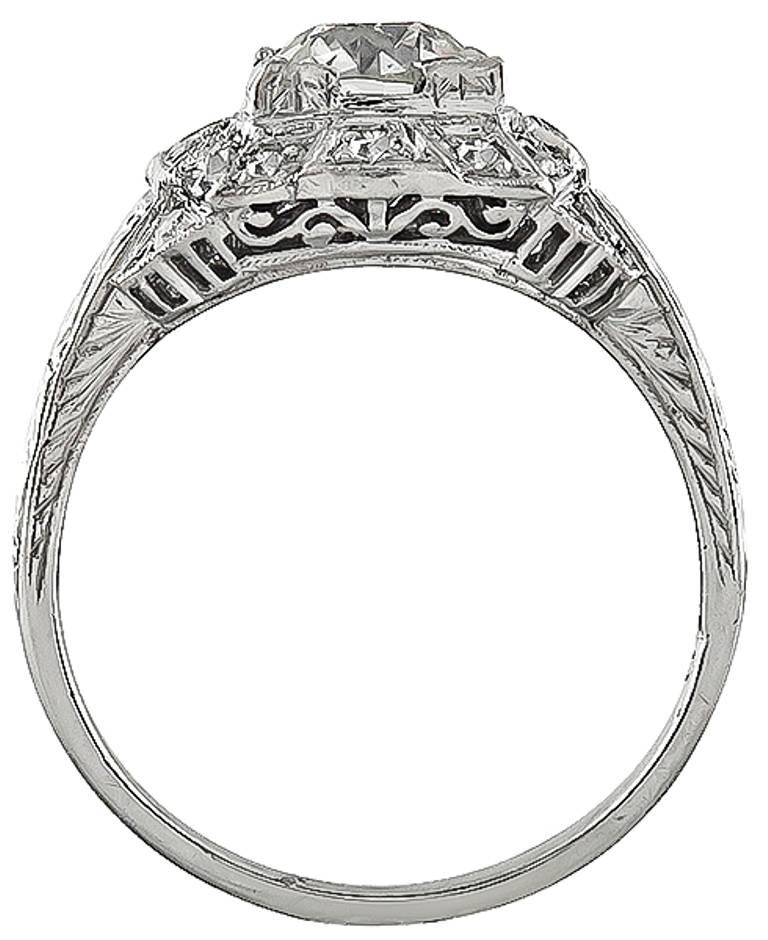 Este asombroso anillo de compromiso de platino de la época Art Déco está centrado con un resplandeciente diamante de talla brillante europeo antiguo certificado por el GIA que pesa 1,02 ct. graduado en color K con claridad VS2. Acentuando la piedra