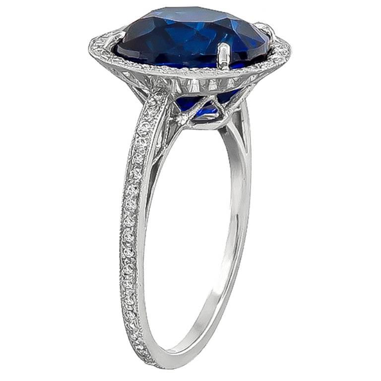 Made of platinum, this ring is centered with a natural cushion cut sapphire that weighs approximately 5.50ct. The center stone is accentuated by sparkling round cut diamonds that weigh approximately 0.50ct. graded H color with VS clarity. The ring