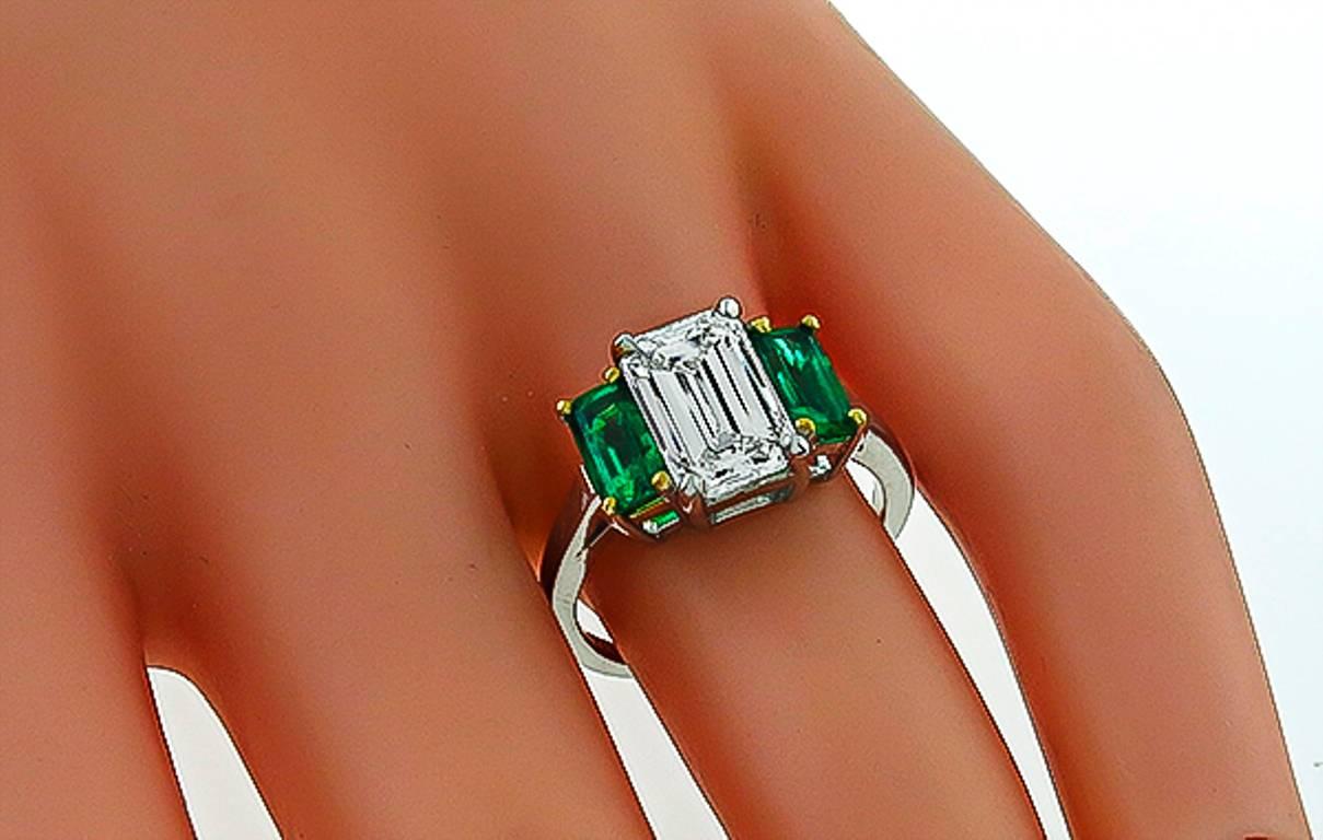 This elegant platinum engagement ring is centered with a sparkling GIA certified emerald cut diamond that weighs 2.27ct. and is graded H color with SI1 clarity. The center diamond is flanked by two emerald cut Colombian emeralds that weigh