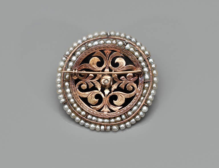 A circular brooch in gold, onyx and pearls, with geometrical detail in platinum and diamonds and central pearl.

Central pearl measures approximately 0.50 cm

Unmarked