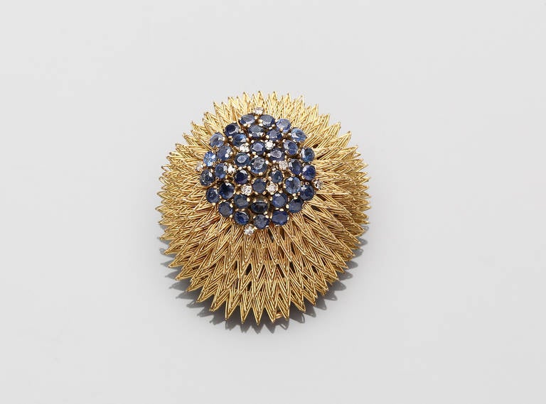 Composed of a pair of earrings and brooch of circular format with a central cluster of sapphires and diamonds.

Brooch measures approximately 4 cm in diameter.

Earrings measure approximately 2 cm in diameter.  

Marked 18K