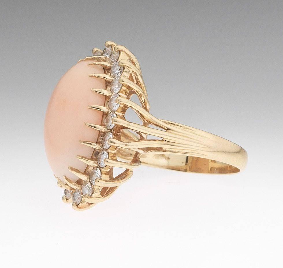 Striking 14k yellow gold ring set with an oval angel skin coral cabochon, measuring 17.20mm x 10.09mm, and surrounded by round brilliant cut H/VS diamonds, total estimated diamond weight 1.00 carats.  The overall weight is 6.8 grams.  The ring