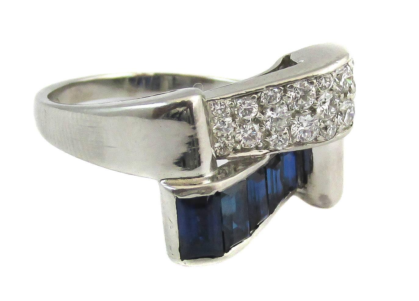 This Retro ring features five deep blue sapphire baguettes weighing approximately 1ct total and 18 round brilliant cut diamonds totaling 0.5cts. Typical for the Retro style that takes in reference form the geometric inspired Art Deco period, the