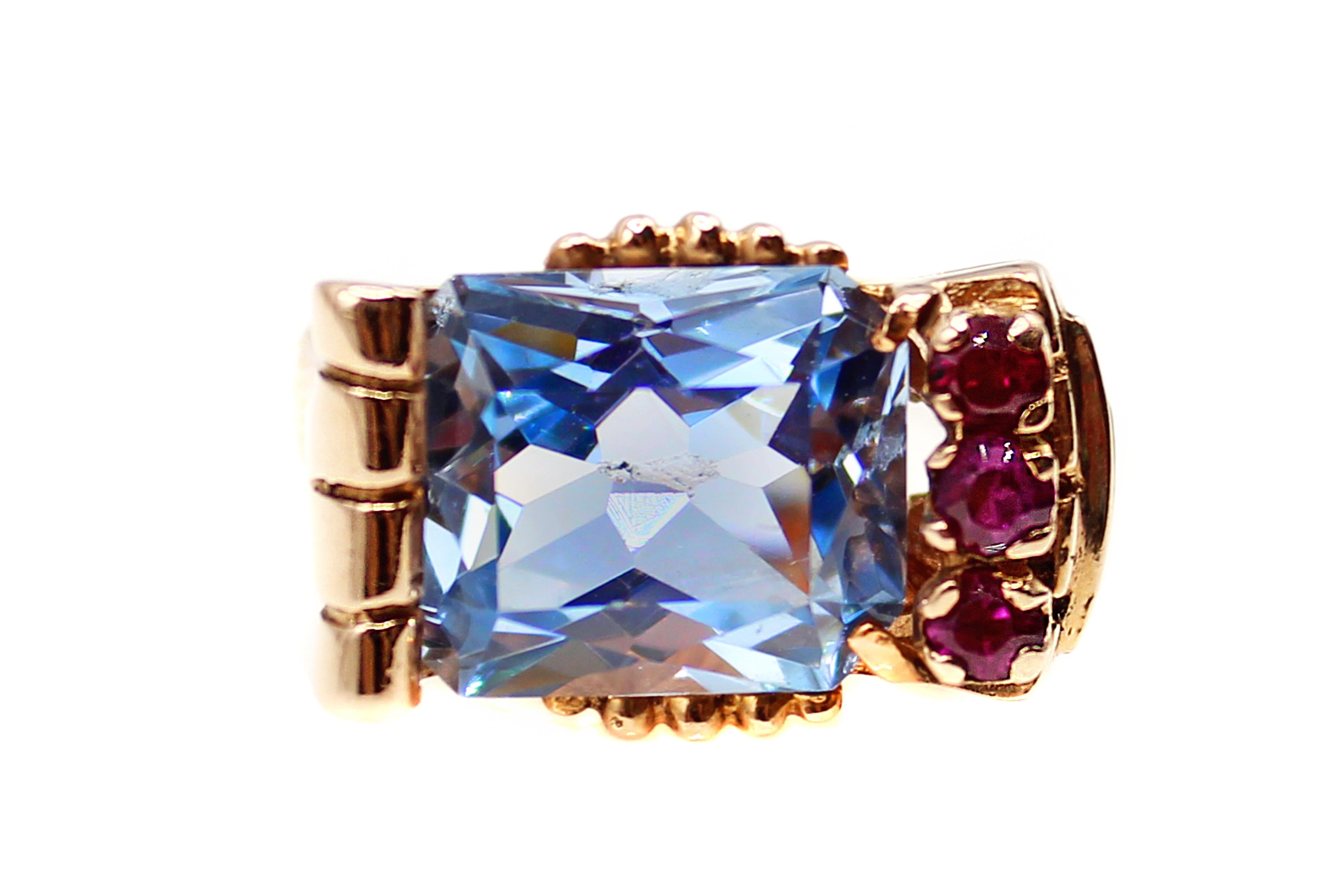 Uniquely designed as an asymmetrical interesting ring, this creation from ca 1940 is masterfully hand-crafted in rose gold. This charming Retro ring features a centrally horizontally set carre cut Aquamarine and is embellished by 3 bright red
