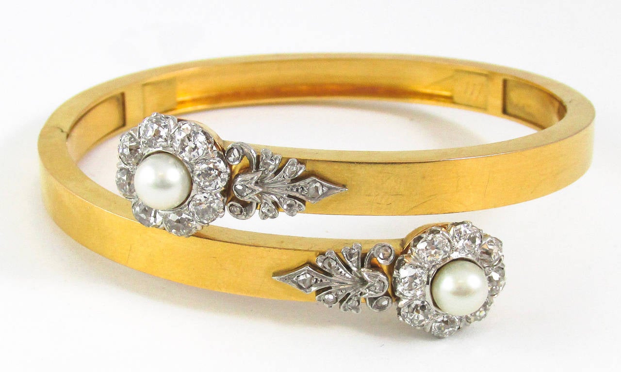Beautifully crafted in 18 karat yellow gold, this wrap bangle is finished with elegant platinum elements that are embellished with lovely rose cut diamonds. Each end of the bangle holds a luminous natural saltwater pearl which that is surrounded by