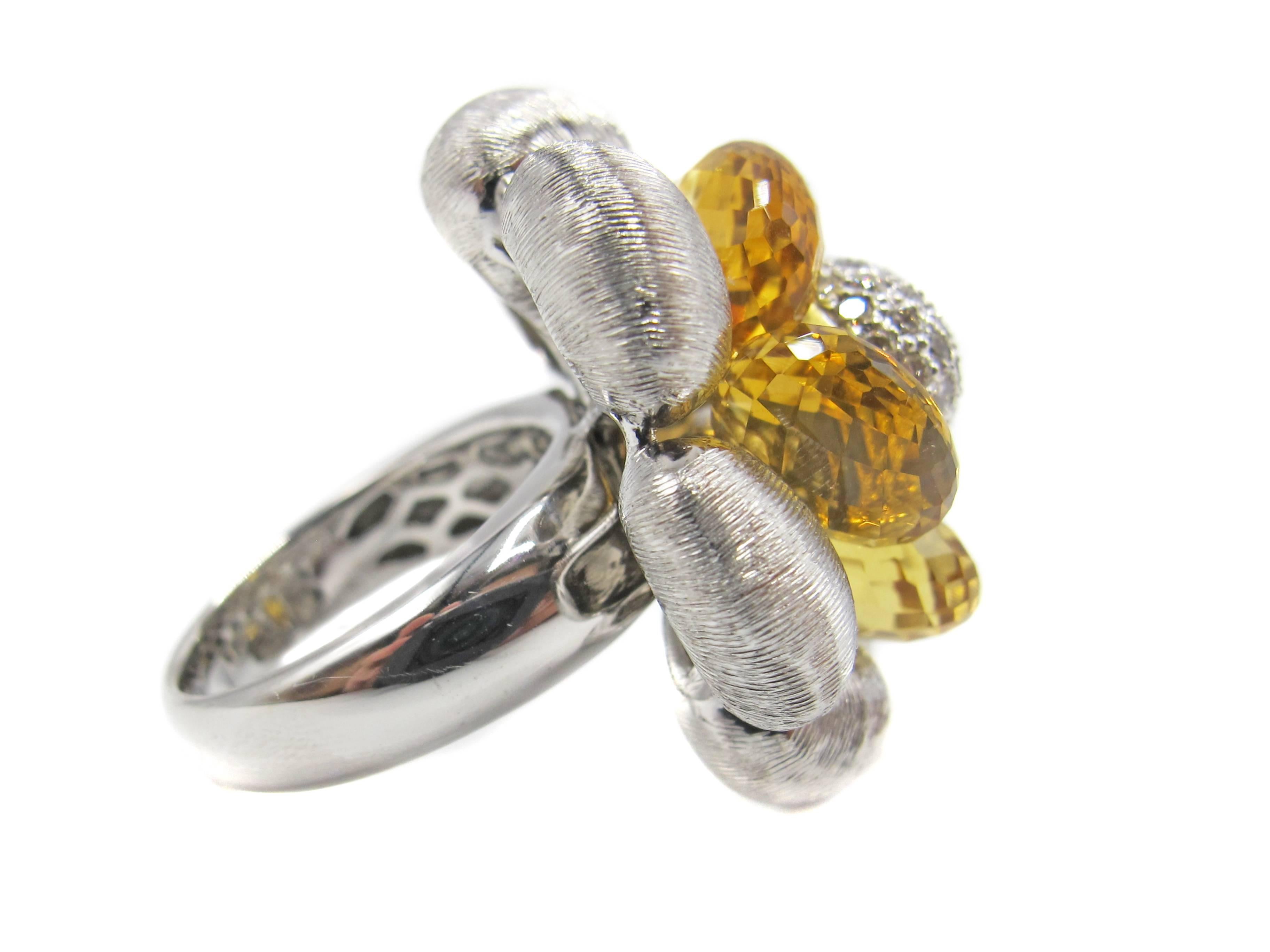 Fun and extravagant Citrine and diamond flower blossom ring hand crafted out of 18 karat white gold.The ring is designed with 7 curved and ribbed petals surrounding a blossom of 5 gold color Citrine briolettes. The briolettes are connected by a wire