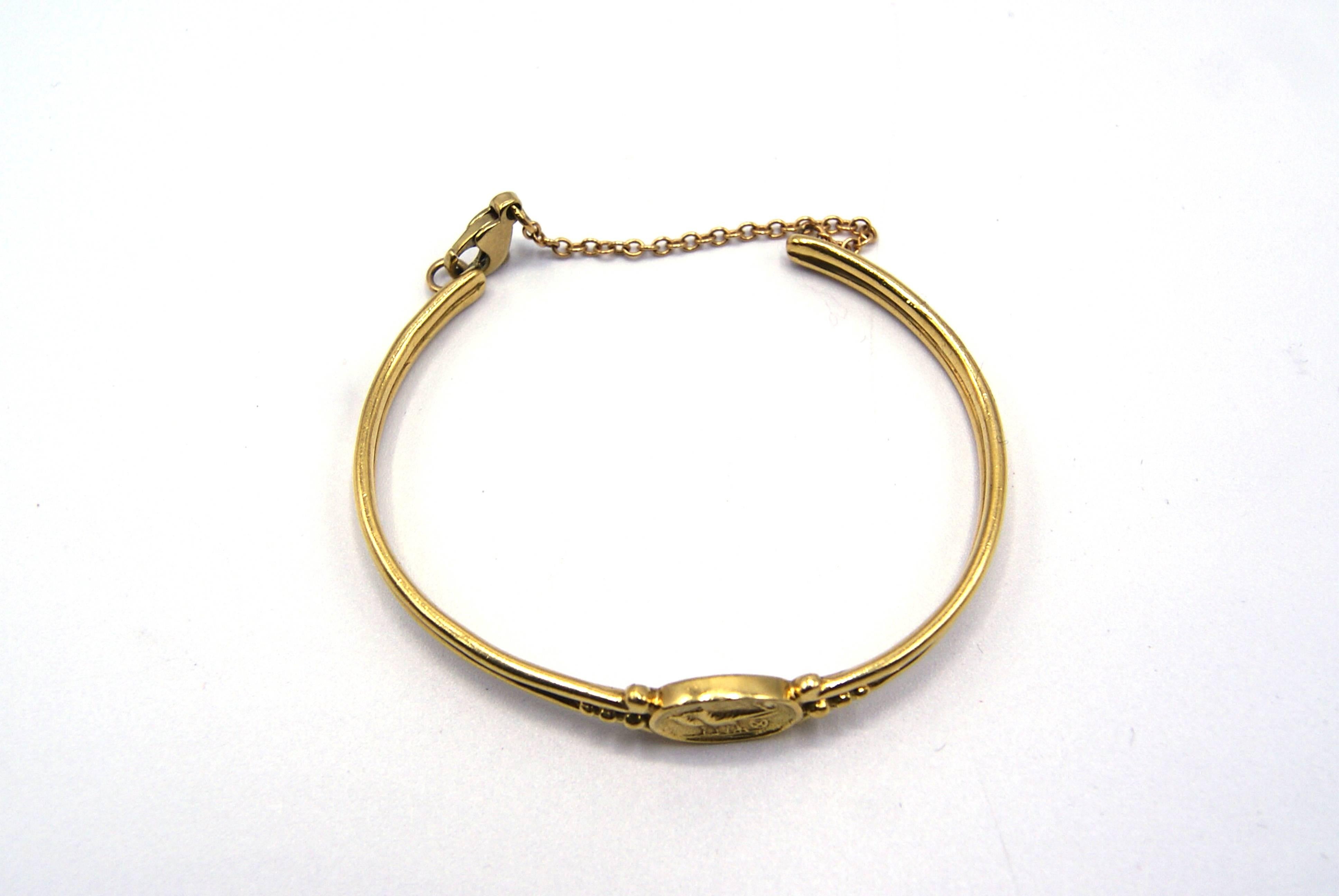 Beautifully 18 karat yellow gold bangle bracelet by New York jewelry designer Helen Woodhull. This bangle is from Woodhull's Egyptian Revival collection and the center plaque resembling an ancient coin with a pair of Ravens. Helen Woodhull has a