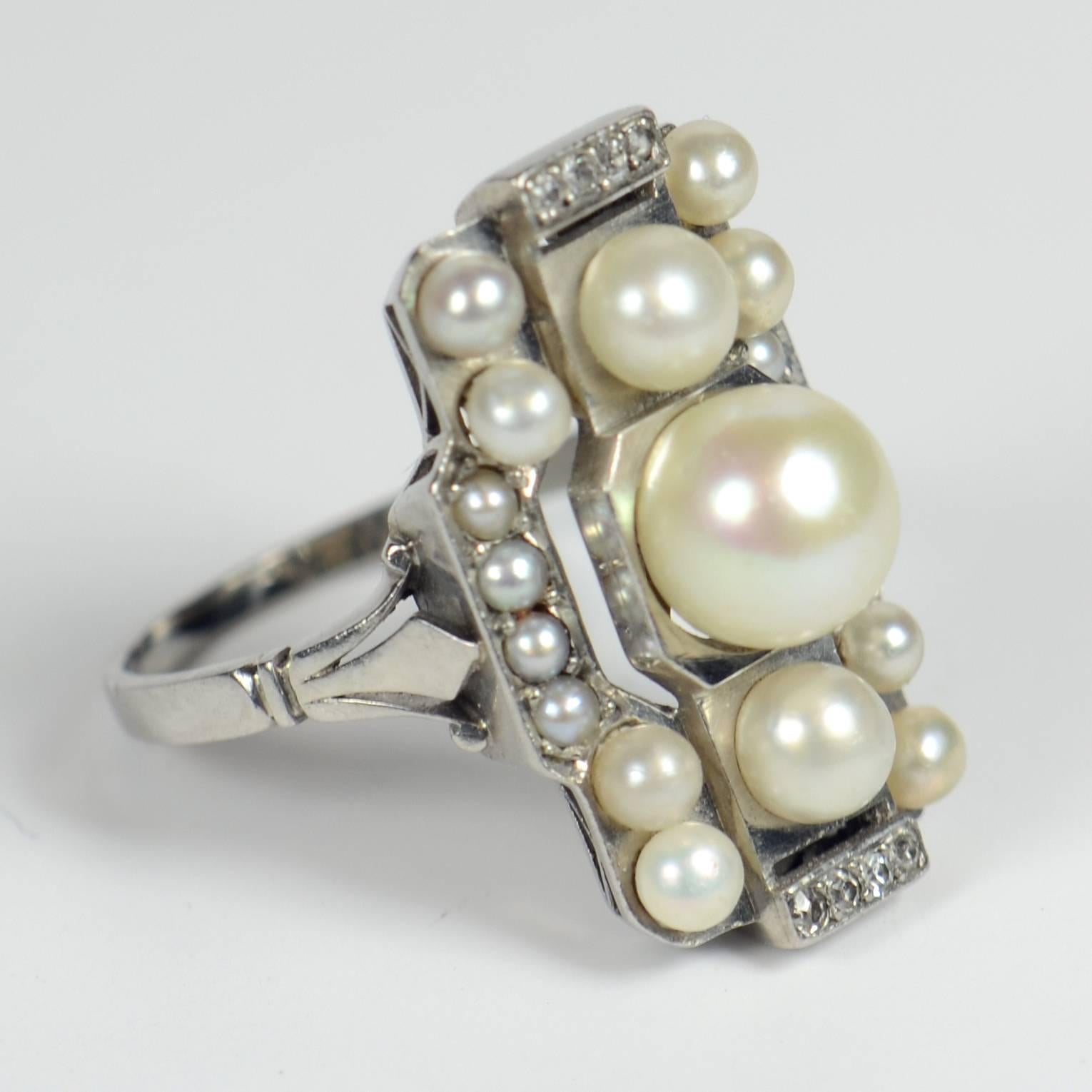 An elegant French Art Deco ring in platinum set with natural white saltwater pearls and diamond accents. The slim shank meets the top of the ring with fleur-de-lis shoulders and is marked with the French import stamp for platinum.  

The ring is set