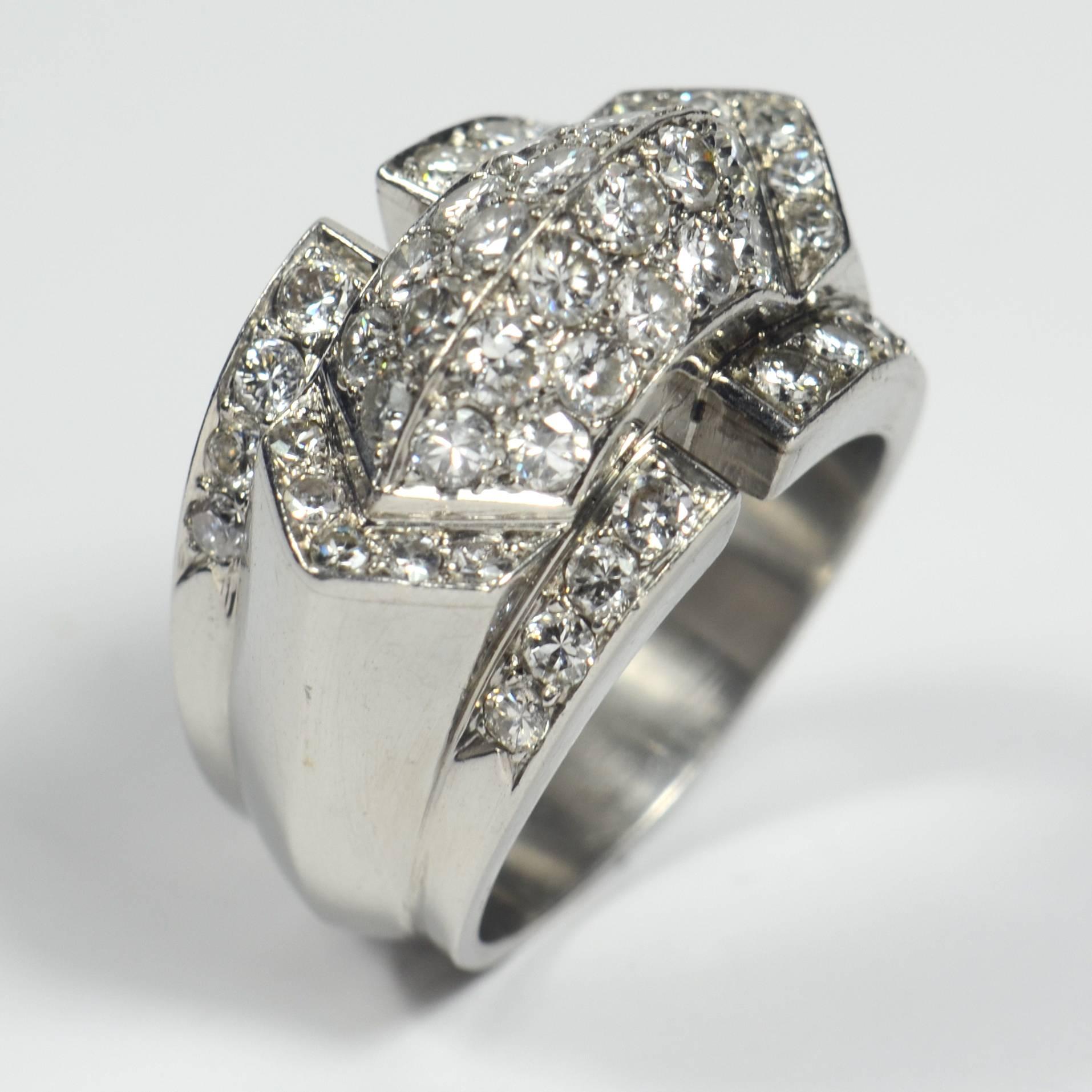 An immensely stylish platinum ring with architectural and geometric forms surmounted by a ridged diamond pavé-set bridge rising from a triangular shaped base inset with single cut diamonds. The shank tapers away from the top of the ring while