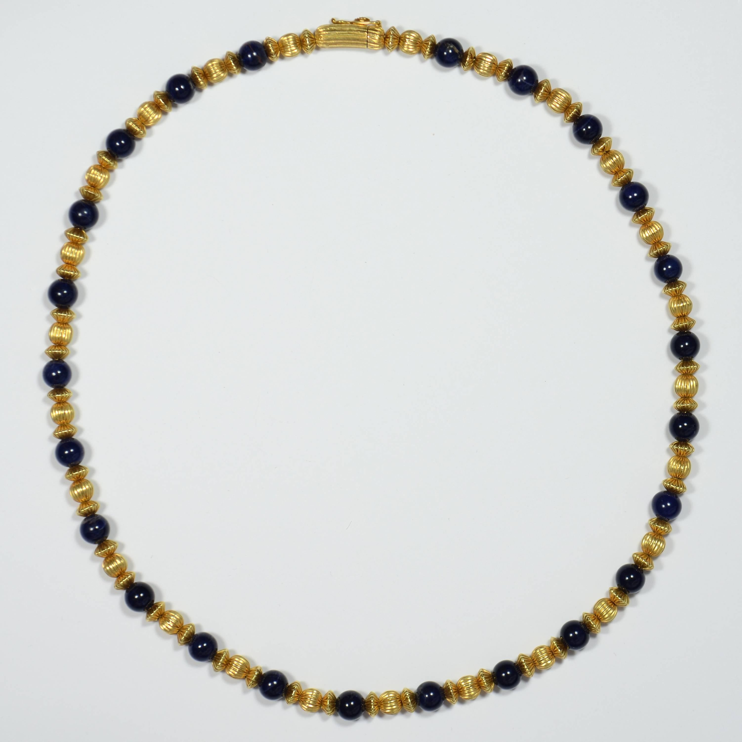 An 18 carat yellow gold necklace by Greek designer Ilias Lalaounis, with 24 dark blue sodalite beads each interspaced by 3 round and saucer shaped fluted gold beads. The beads are strung on a gold foxtail chain.

The clasp is marked ‘GREECE’, 750