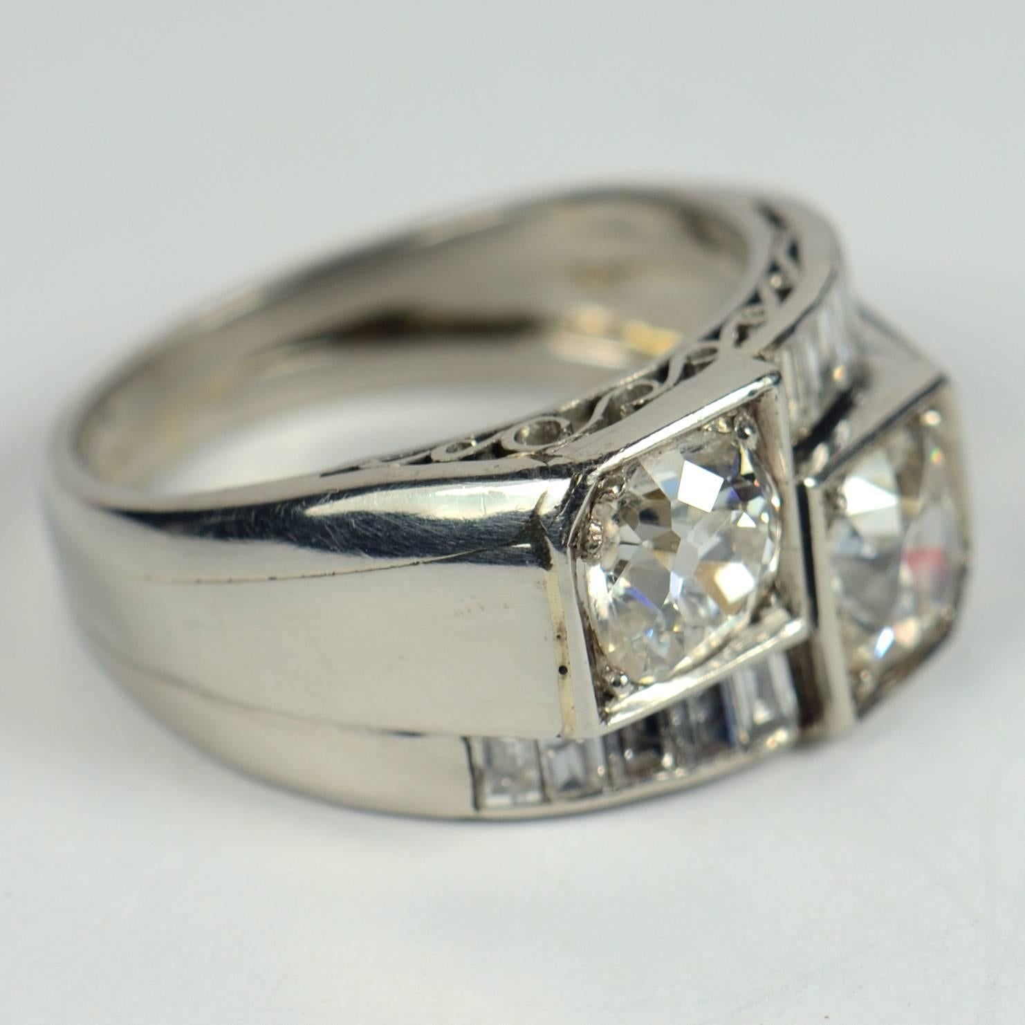 This late Art Deco ring is set with two old European-cut diamonds each weighing approximately 1.00 carats with I-J colour and Pique (included) clarity.  The diamonds are mounted in a geometric platinum setting, with alternating shoulders giving an