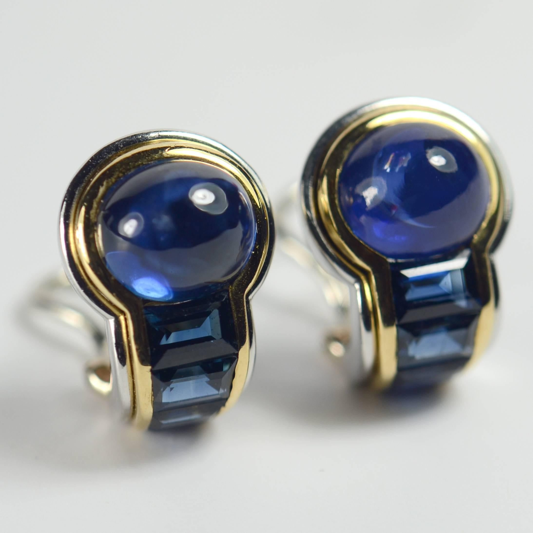 A very chic pair of sapphire earrings mounted in platinum with gold detail by Hemmerle from the 1980s.   Each earring is set with a large oval cabochon sapphire to a tapered line of four emerald-cut and trapeze-cut sapphires.  The earrings have