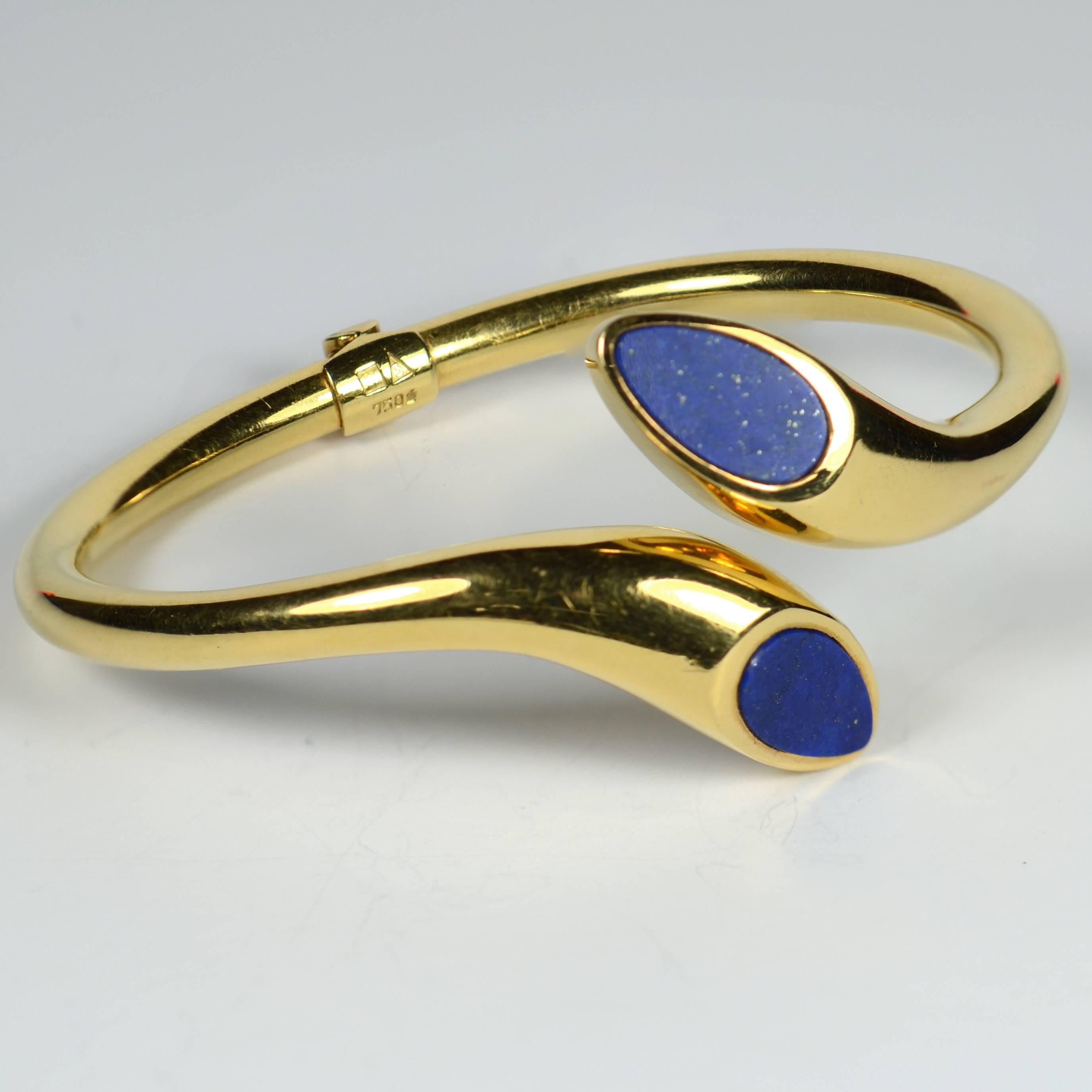 A hinged cuff bangle set with a pear-shaped blue lapis lazuli tablet to each tapered gold terminal. 

The bracelet has an inner circumference of 16.5cm (6.5 inches), with an inner diameter of 5.9cm.

Marked 750 for 18 karat gold. Weight: 32.3g. 
