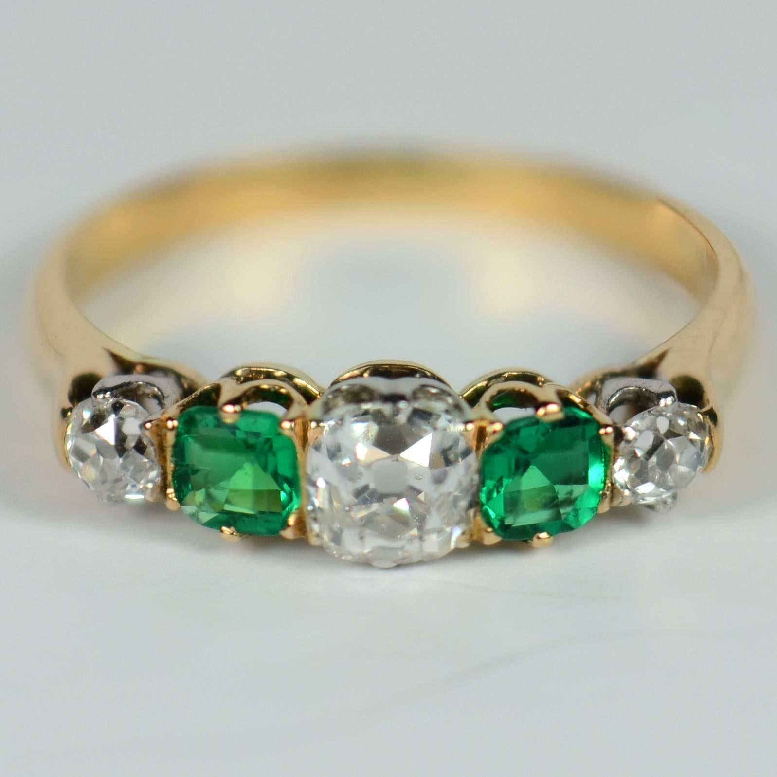 A classic five-stone ring set with two intensely green step-cut emeralds and three bright and lively old-cut diamonds.
The diamonds weigh a total of approximately 0.70 carats and are F-G colour and VS-SI clarity.  The emeralds weigh a total of
