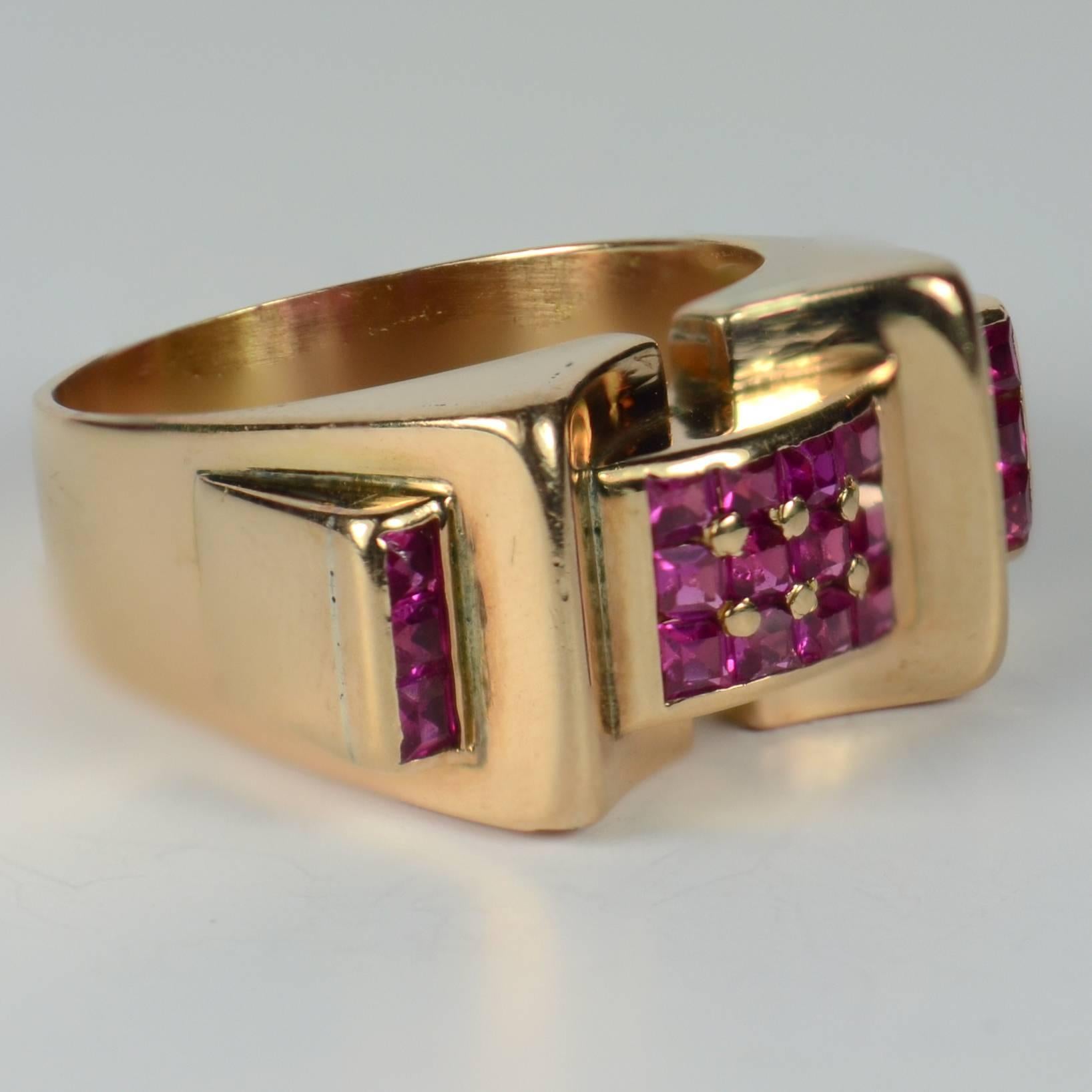 A French 18 carat gold ring in the architectural Retro style set with 18 square cut rubies totalling approximately 0.70 carats in a ‘bridge’ design.  The curve of the bridge section is interrupted by arching gold forms which continue down to form