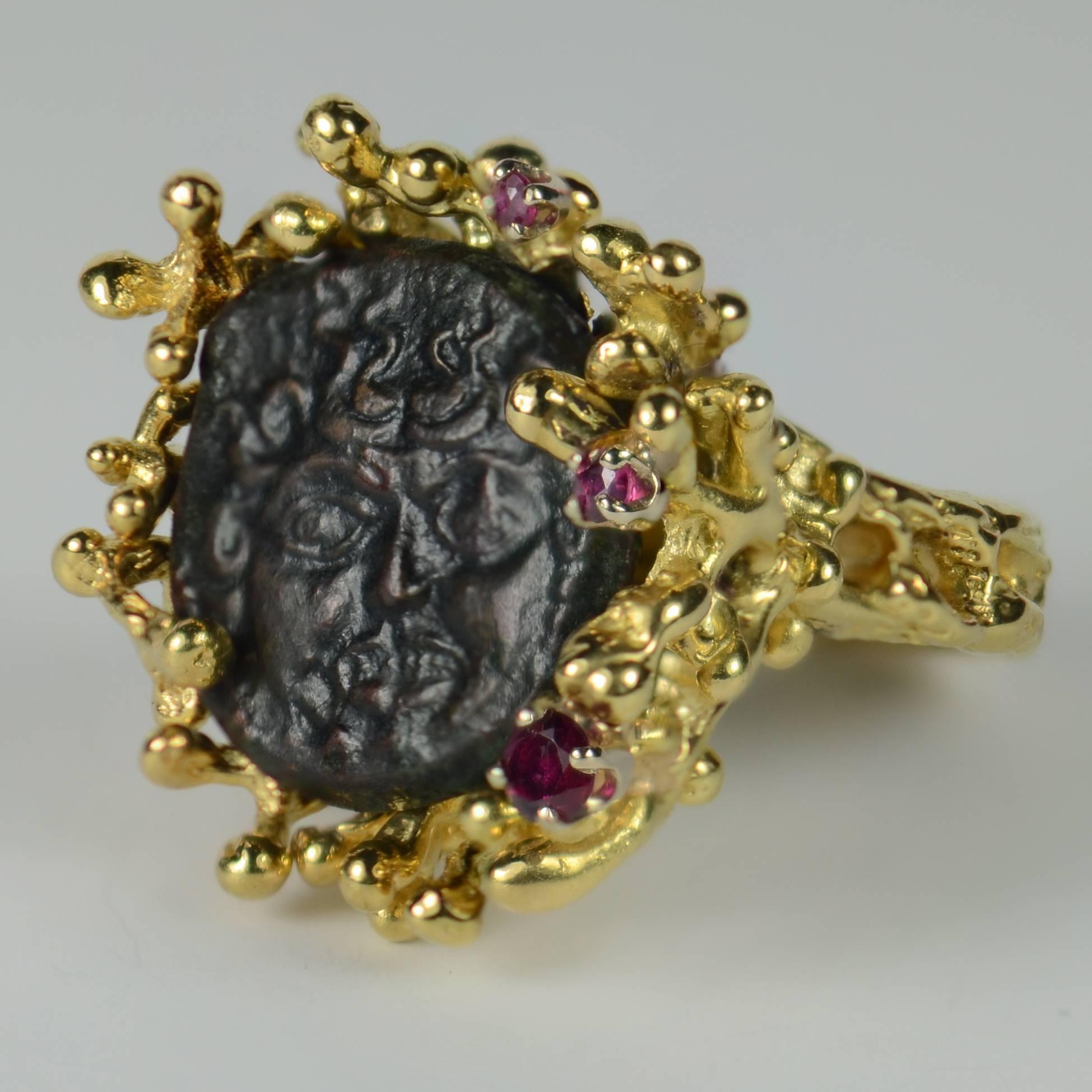 The central point of this unusual ring is an ancient bronze coin with a Medusa face detail.  It is mounted in an organic 18 carat yellow gold mount with 3 asymmetrically positioned natural rubies.  This ring was made circa 1970-1980.

The Medusa