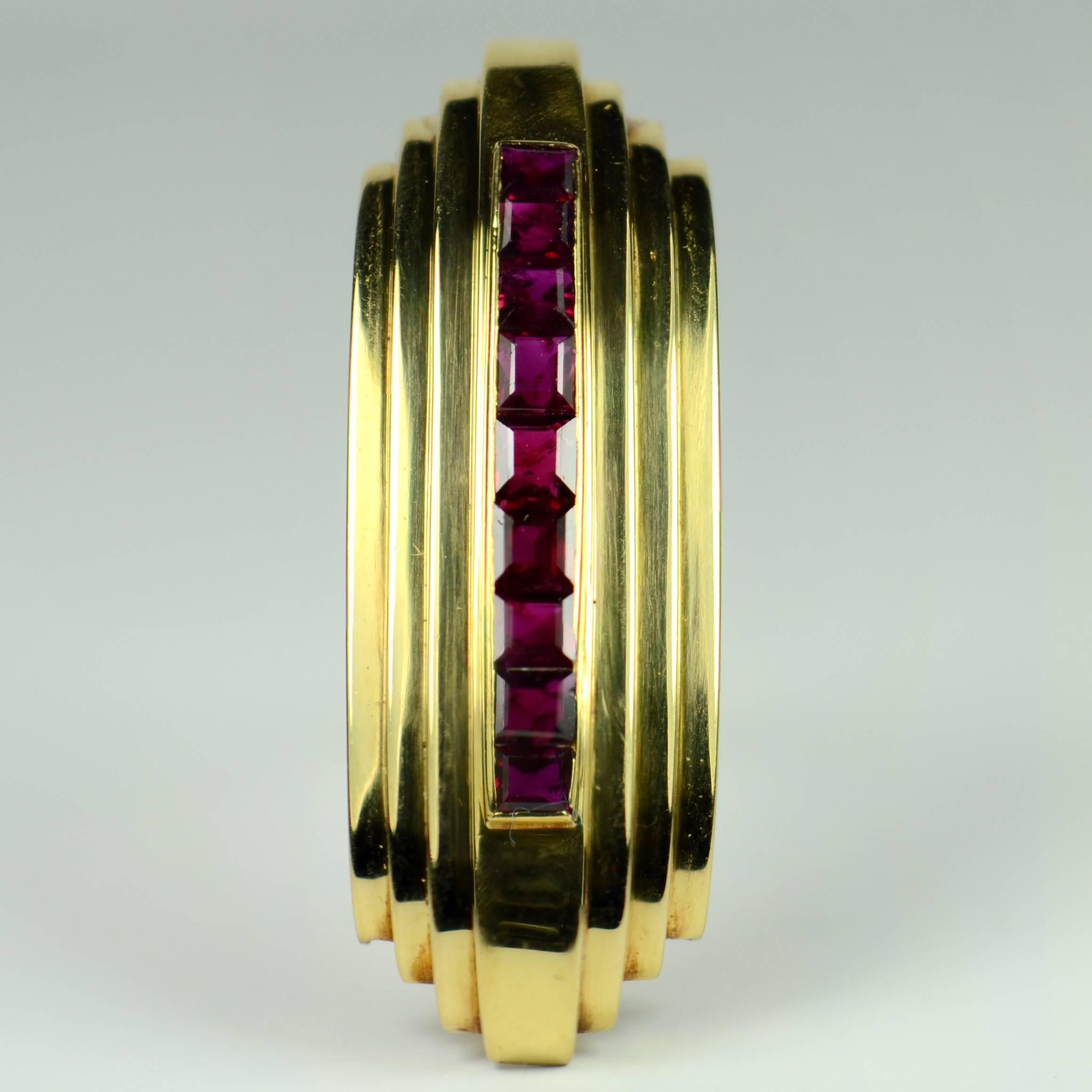 An unmarked 18 carat gold brooch formed as a gently curving arch with three steps up to the central panel which is channel set with 9 step cut rubies.

The clean lines of this design accompanied by the 3-dimensional curved form anchors this brooch