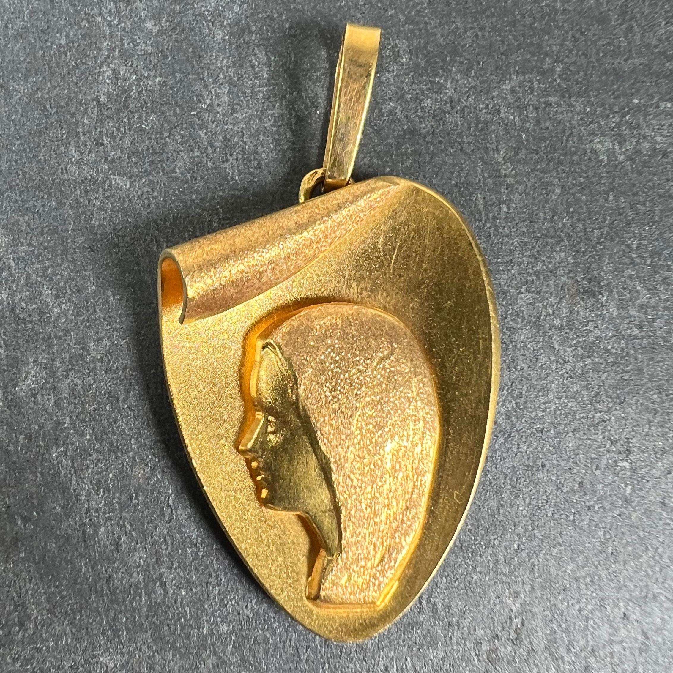 Pendentif français en or jaune 18 carats (18K) conçu comme une médaille en forme de cœur stylisé représentant la Vierge Marie. Estampillé avec la tête d'aigle pour la fabrication française et l'or 18 carats, avec la marque du fabricant pour