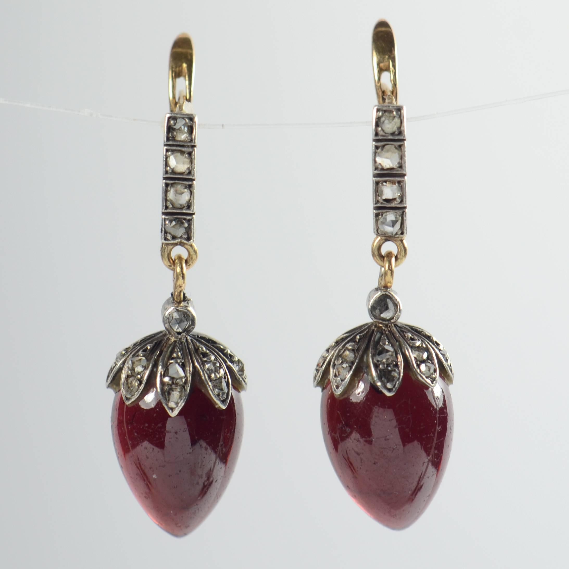 These lovely Victorian earrings date from the 1870s and are designed as pear-shaped garnet pendants topped with diamond leaf forms in a ‘strawberry’ design, suspended from diamond set bars.  

The almandine garnets are cut in a double cabochon (with