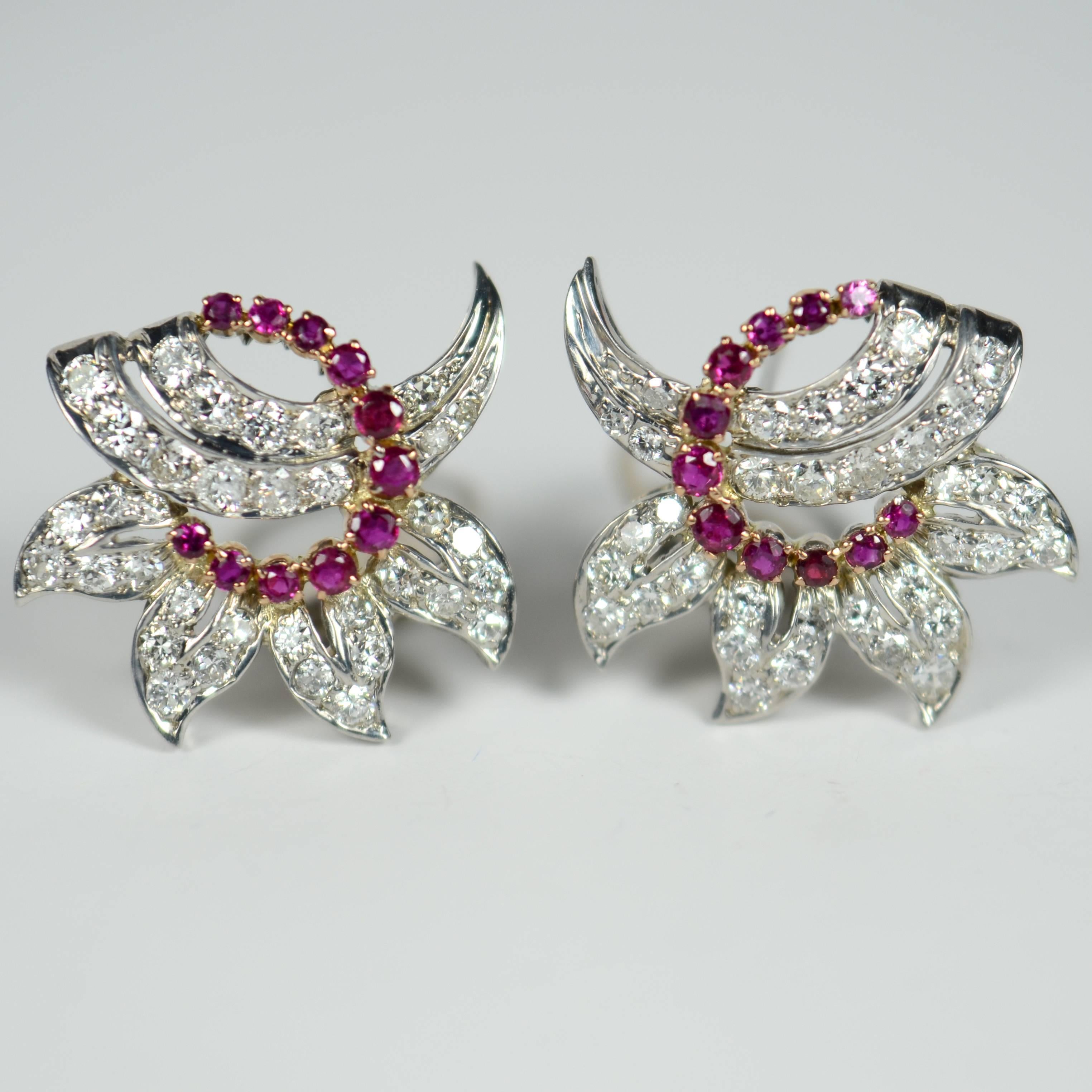 A pair of ruby and diamond ear clips designed as stylised diamond flowers with an intricate cut out design and a swirl of rubies.

 The rubies are set in 18 carat yellow gold and the diamonds are mounted in 18 carat white gold. 

The 22 natural
