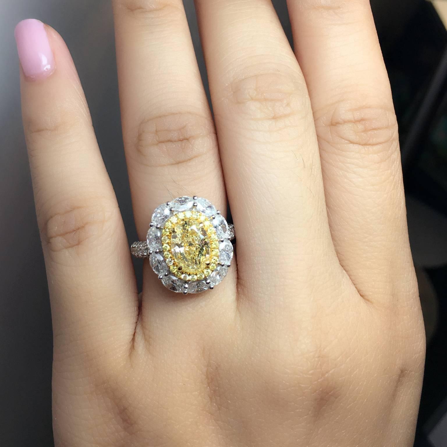 Fancy Yellow 2.11 Carat Oval cut diamond and VS2 clarity center stone. Surrounded by a row of 0.20 carat of yellow diamonds and 10 oval diamonds around the row. Small round brilliant diamonds on the band weighing 0.56 carat. Made in 18K gold. Ring